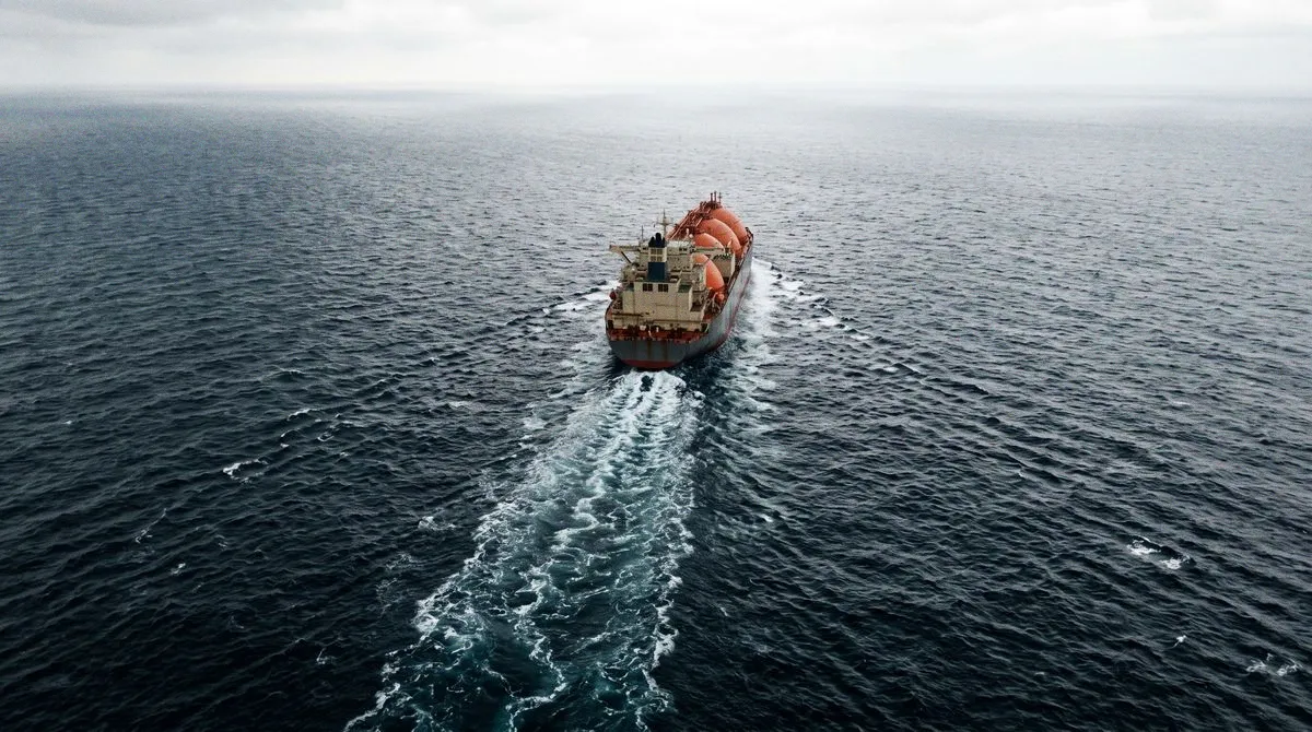 Un buque metanero con tanques esféricos, solo en mar abierto, visto desde arriba; su estela recta llega hasta el borde inferior de la foto